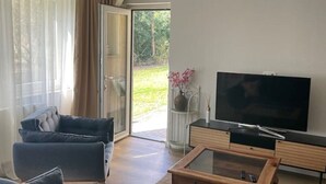 Ein modernes Wohnzimmer mit einer Couch, einem Couchtisch, einem Fernseher und einer Schiebetür zu einem Garten.