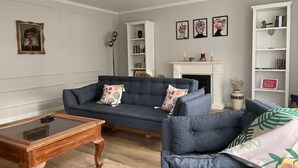 Ein Wohnzimmer mit einem dunkelblauen Sofa, einem Holztisch, einem weißen Kamin und einem Bücherregal.