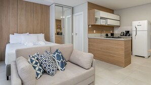 Moderni hotellihuone, jossa on sohva, sänky, pieni keittiö ja kylpyhuone.