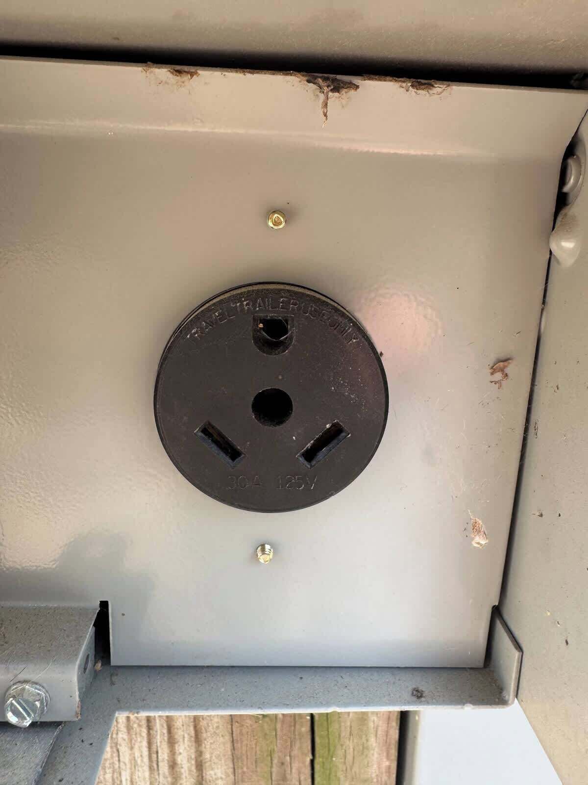 Ein metallisches Stromdosenfach mit einer runden Steckdose, einer Schraube und einem Etikett mit der Aufschrift '30A 125V'.