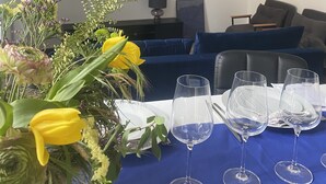 A living room with a TV, blue sofa, and a table with wine glasses and flowers. - 􏰇􏰅􏰱􏰂􏰄􏰎􏱂􏰳􏱃 􏰄􏰁􏰁􏰂􏰅􏰇􏰁􏱂􏰃􏱃appartement Dans le Centre Historique (Lourdes)
