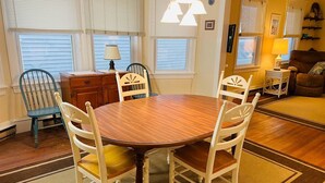 A dining area with a round wooden table and four white chairs, a wooden cabinet, and a lamp.