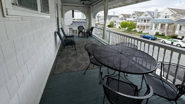 A covered porch with a table and chairs, overlooking a residential street.