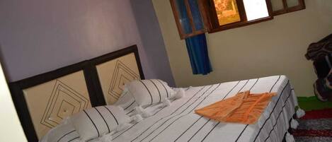 A bed with striped bedding and a decorative headboard, a window with curtains, and a partial view of a staircase.