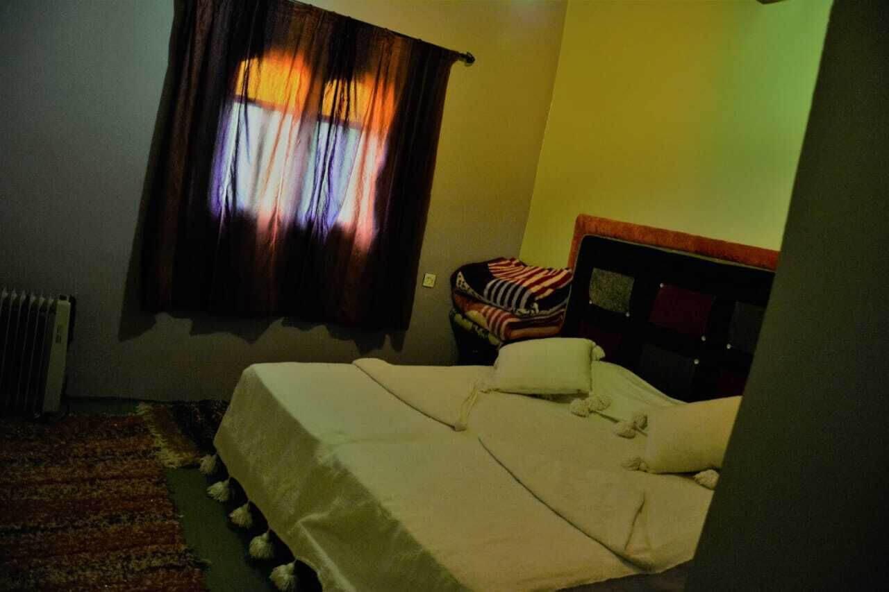 Een kleine, schemerige kamer met een enkel bed, een radiator en een raam met gordijnen.