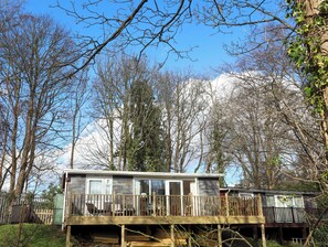 A cabin with a deck, surrounded by trees and a mountain in the background. - Treetops (Caernarfon)