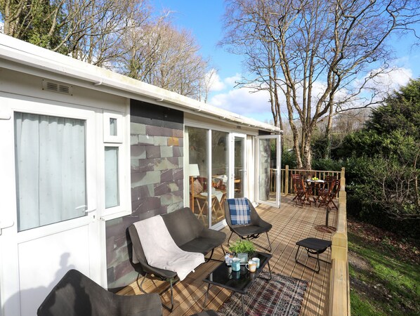 A mobile home with a patio area featuring outdoor seating and a table. - Treetops (Caernarfon)