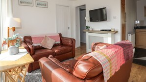 Una sala de estar con un sofá de cuero marrón, una mesita de madera y un televisor montado en la pared.