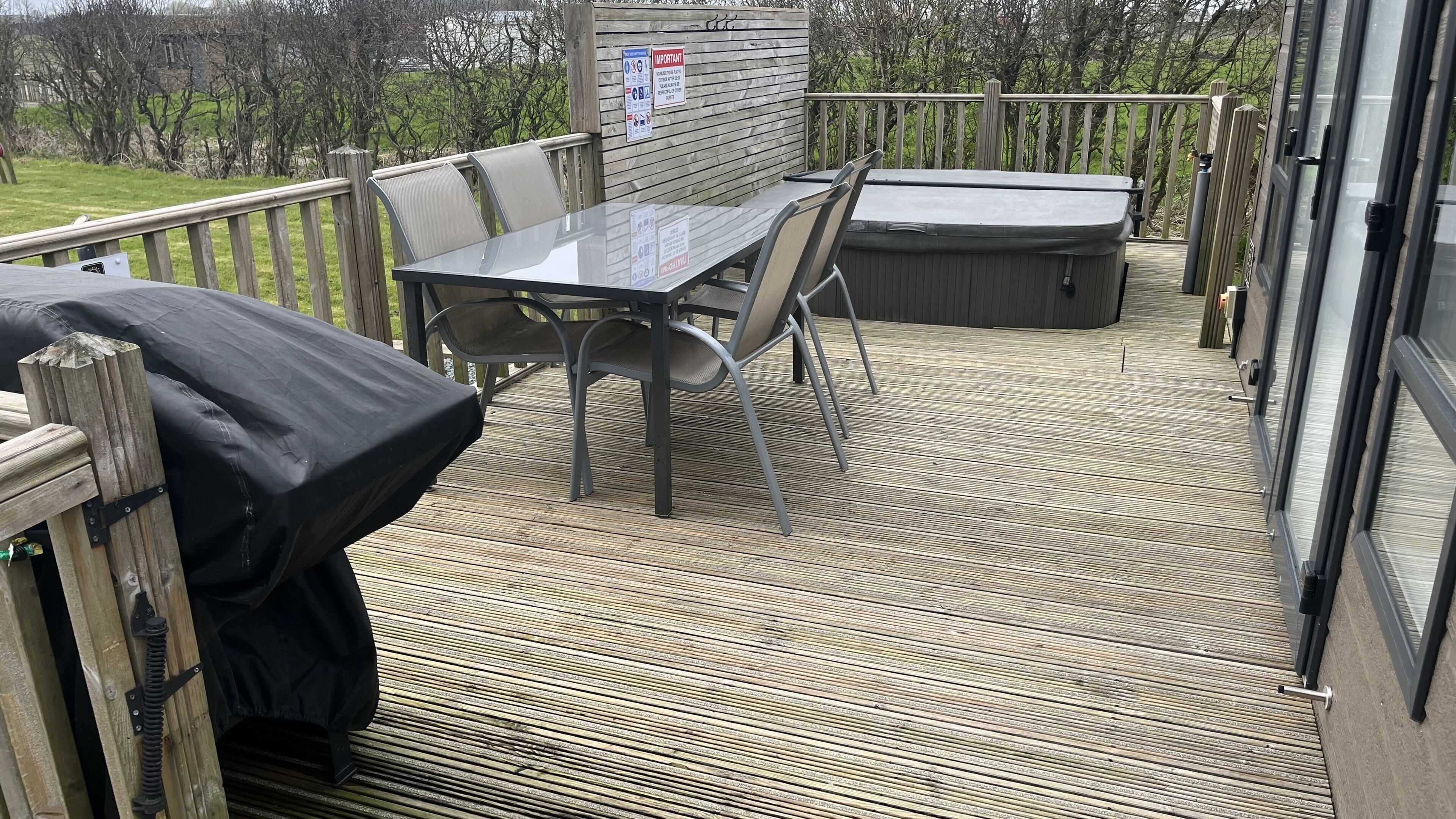 A covered outdoor deck with a table and chairs, a hot tub, and a wooden railing.