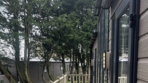 A wooden deck with a metal railing, leading to a building with large windows. - Cosy 3-bed hot tub Lodge in Pr3 (Preston)