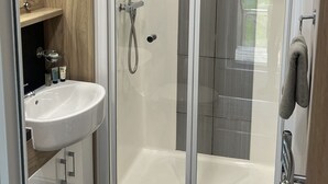 A modern bathroom with a glass-enclosed shower, a white sink, and a wooden vanity. - Cosy 3-bed hot tub Lodge in Pr3 (Preston)