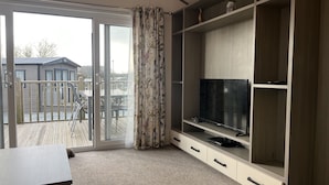 Una habitación con una televisión sobre un mueble de madera, una puerta corrediza de vidrio a un balcón y piso alfombrado.