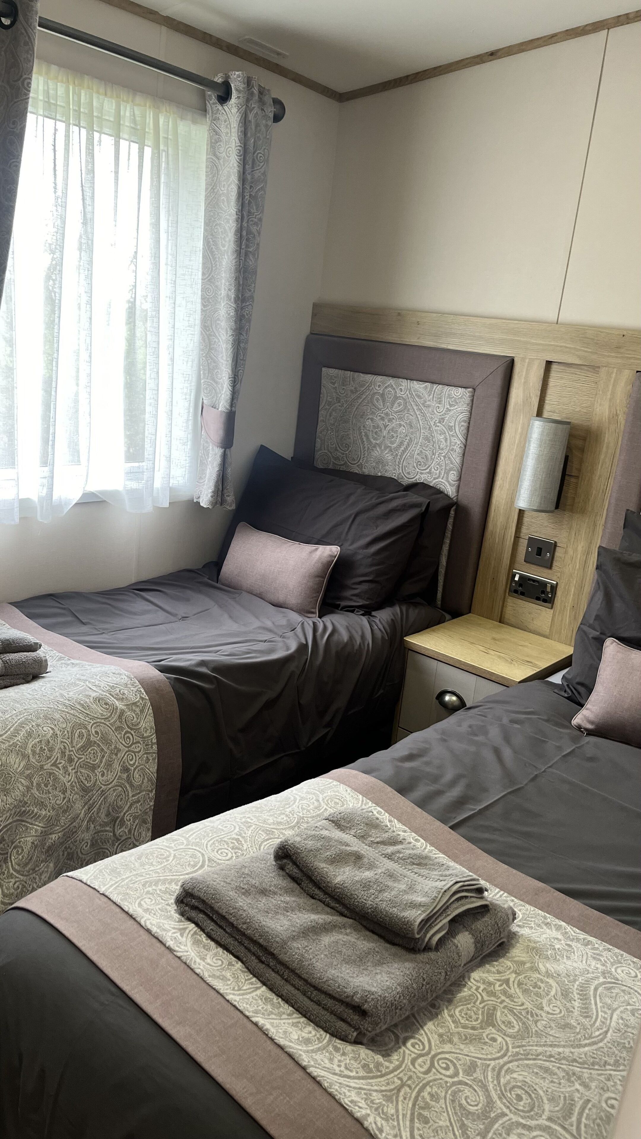Hotellihuone, jossa on kaksi sänkyä, yöpöytä lampun kanssa ja ikkuna, jossa on verhot.