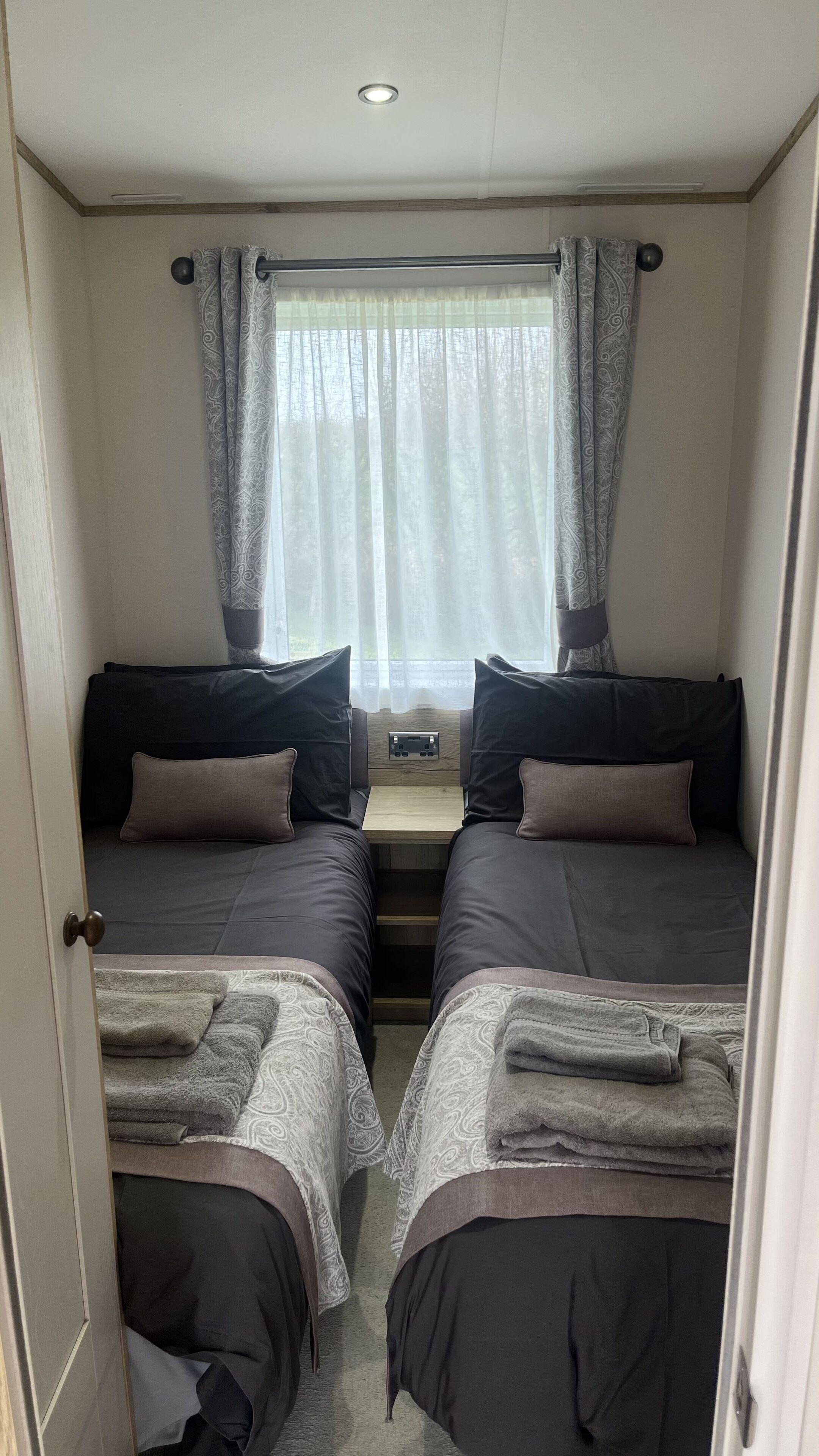 A compact room with two beds, a small table, and a window with curtains.