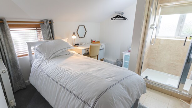 Ein Schlafzimmer mit Bett, Schreibtisch, Stuhl und einer Duschkabine.