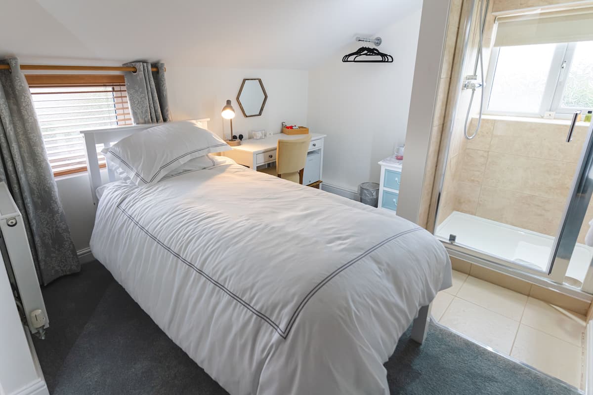 A bedroom with a bed, desk, chair, and a shower area.