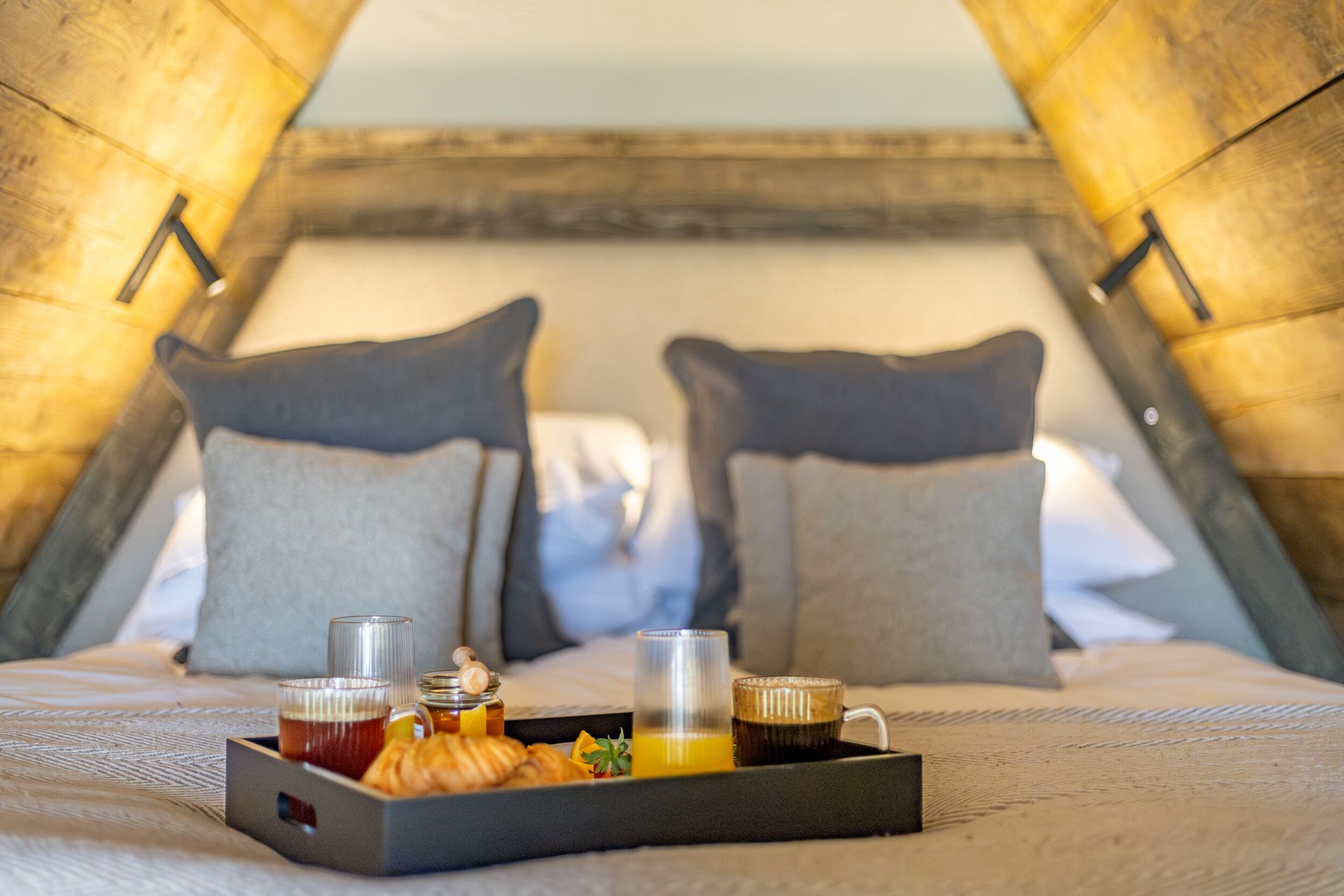 A cozy room with a bed, pillows, a tray with breakfast items, and a cup of coffee.