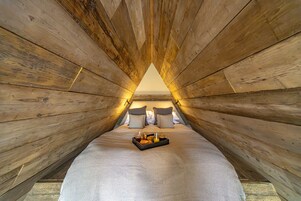 A cozy attic bedroom with wooden walls, a neatly made bed, and a tray of breakfast items.