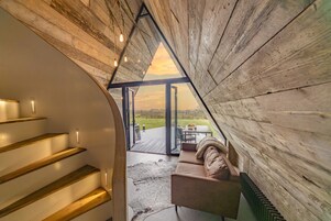 A wooden interior with a staircase leading to a balcony overlooking a grassy area.