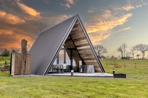 A modern, triangular-shaped building with a sloped roof, a wooden exterior, and a patio area with outdoor furniture.