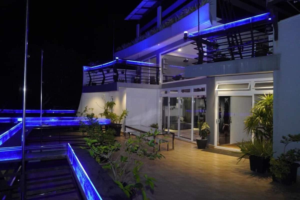 A modern building with a glass entrance, outdoor seating area, and blue lighting.