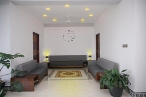 Una sala de estar moderna con un sofá gris, dos mesitas de noche con lámparas, un tapete decorativo y un ventilador de techo.