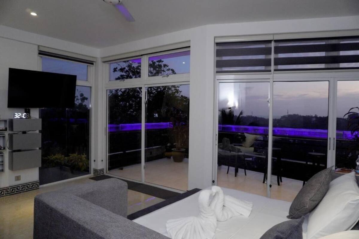 A modern hotel room with a large bed, a flat-screen TV, and a balcony with a view of the city.