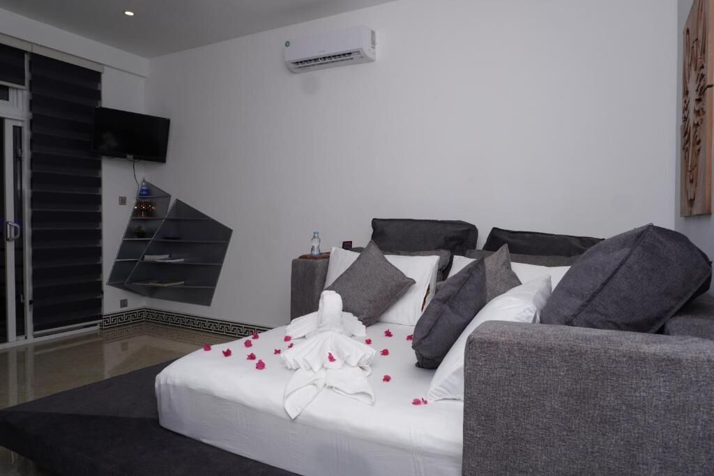 A modern hotel room with a bed, grey sofa, and a TV mounted on the wall.