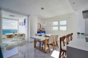 Une cuisine moderne dotée d’un îlot central, d’un coin repas séparé par une cloison en verre et offrant une vue sur la mer.