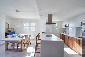 A modern kitchen with white cabinetry, a central island, and a dining area with a white table and chairs. - Exquisite Apartment in Marbella (Playa Juan Dolio)