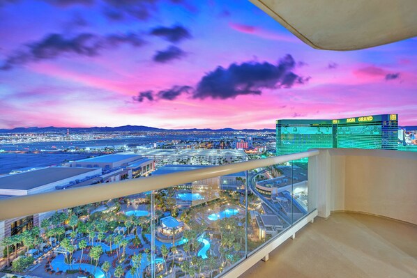 A panoramic view of a resort with a pool area, a large building with a sign, and a sunset sky.