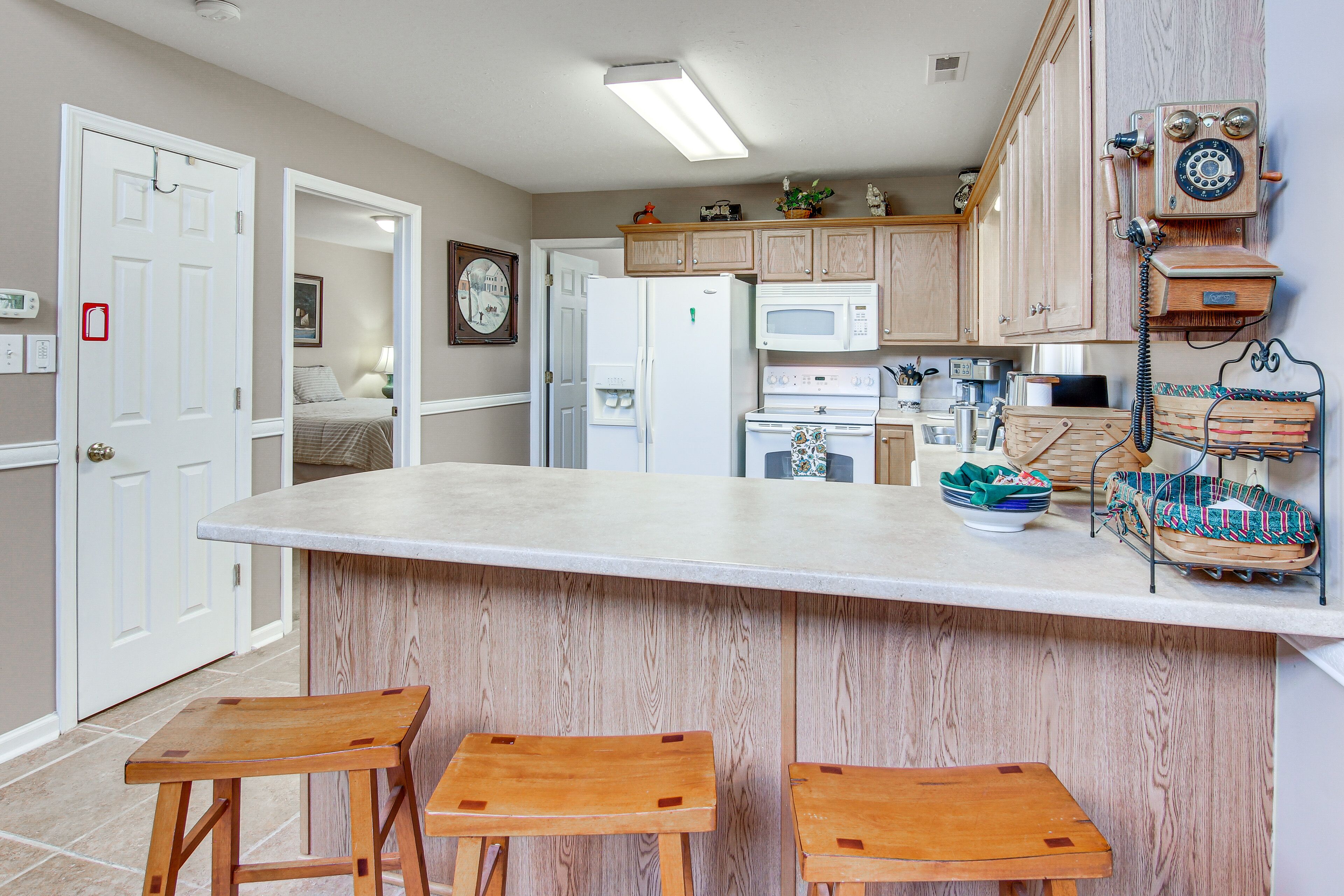 Une cuisine avec des meubles de rangement en bois, un réfrigérateur blanc, un four à micro-ondes et un tabouret de bar en bois.