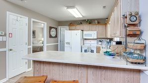 A kitchen with wooden cabinets, a white refrigerator, a microwave, and a wooden bar stool. - 8 Mi to Lake Lure! Mtn-View Gem w/ Furnished Deck (Rutherfordton)