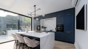 Cozinha moderna com ilha central, armários escuros e uma grande janela com vista para o verde.