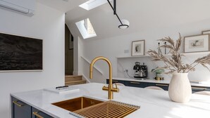 Uma cozinha moderna com bancada de mármore branco, torneira dourada e armários azul-escuros.