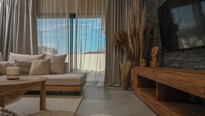 A modern living room with a sofa, a coffee table, and a TV on a stone wall. - Experience life again at Soul Luxury Villa !  (Planos)
