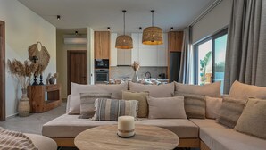 A modern living room with a large beige sectional sofa, a round wooden coffee table, and a kitchen in the background. - Experience life again at Soul Luxury Villa !  (Planos)