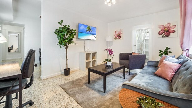 Un salon moderne comprenant un canapé, des fauteuils, une table basse, un téléviseur et des plantes décoratives.