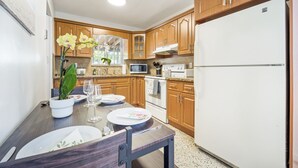 Une cuisine avec des meubles en bois, un réfrigérateur blanc, un four à micro-ondes et une cuisinière. On y trouve une table à manger dressée avec des assiettes, des verres et une plante en pot.