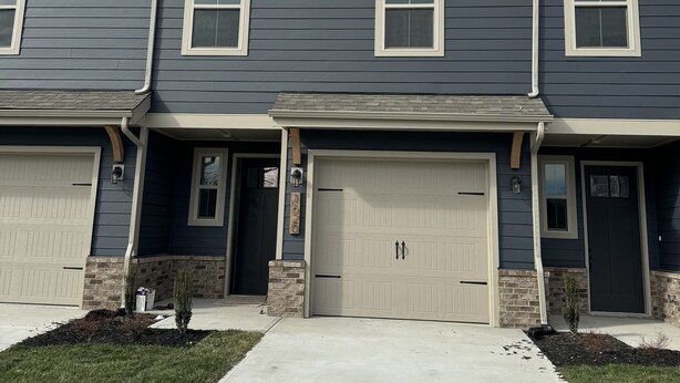 A two-story residential building with a garage, a small front porch, and a clear sky.