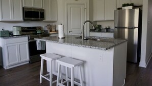 A modern kitchen with white cabinetry, a granite countertop, stainless steel appliances, and a small island with bar stools.