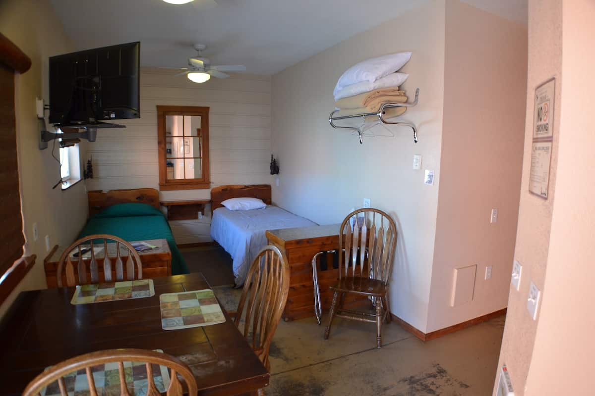 A small, cozy room with a bed, a desk, and a chair. There is a television mounted on the wall and a ceiling fan.