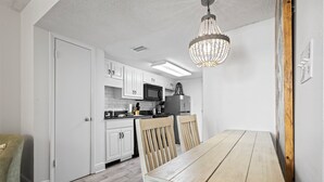A kitchen with white cabinets, a wooden dining table, and a chandelier. - Beach Access, Pool/Hot Tub, Sleeps 5 - Vet Owned (Gulf Shores)