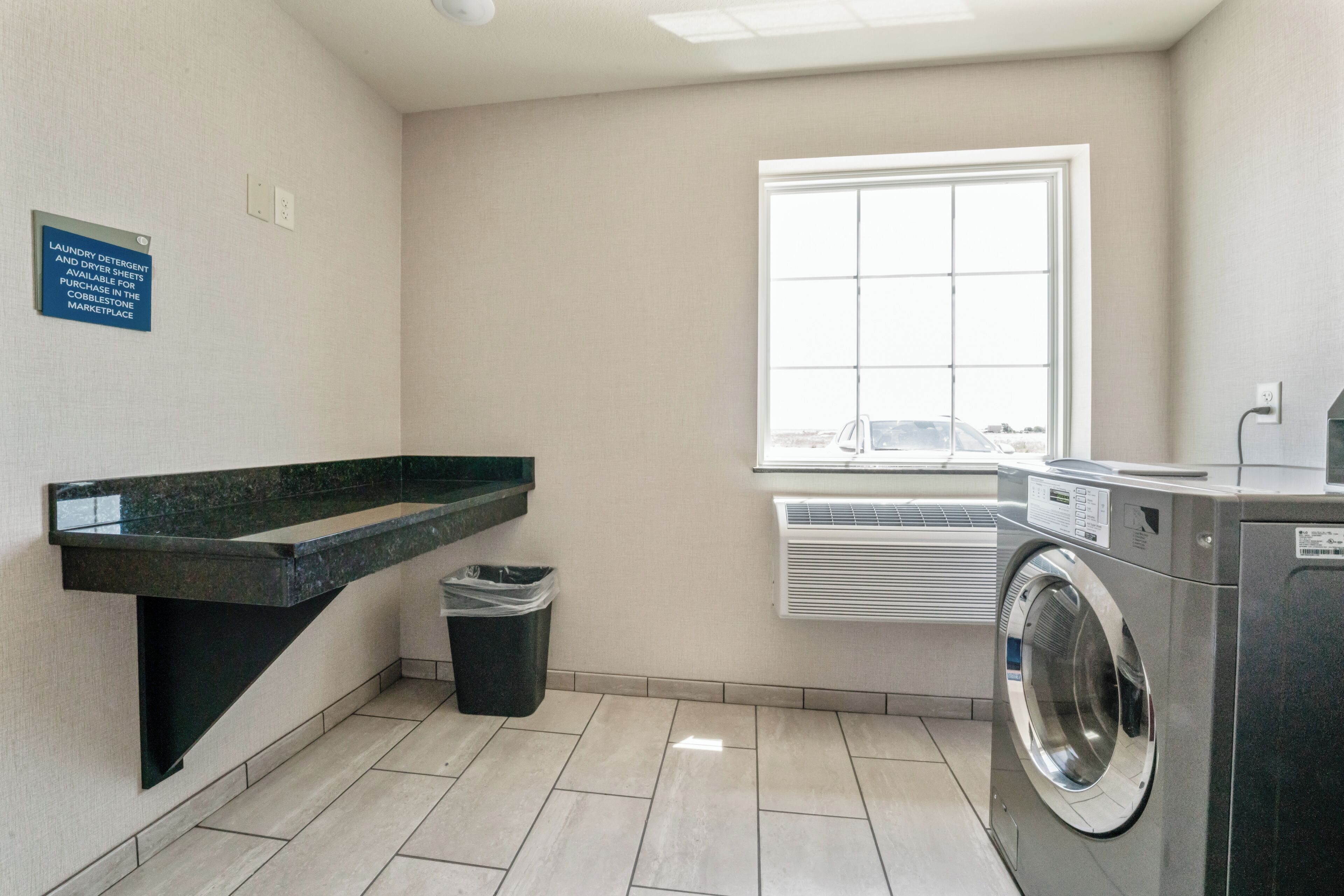 A laundry room with a washing machine, a sink, and a trash bin.