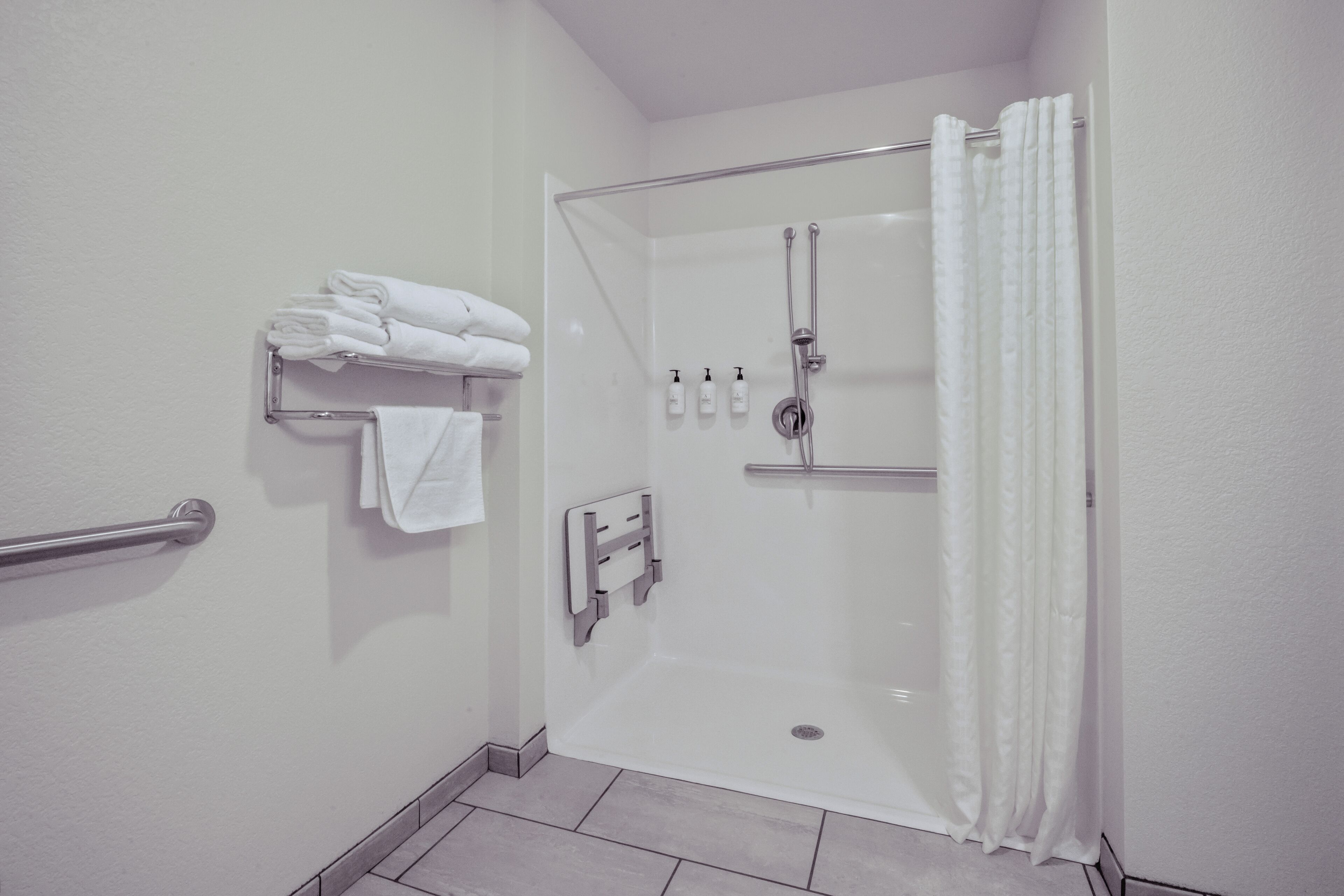 A modern bathroom with a glass-enclosed shower, a towel rack with folded towels, and a hand dryer.