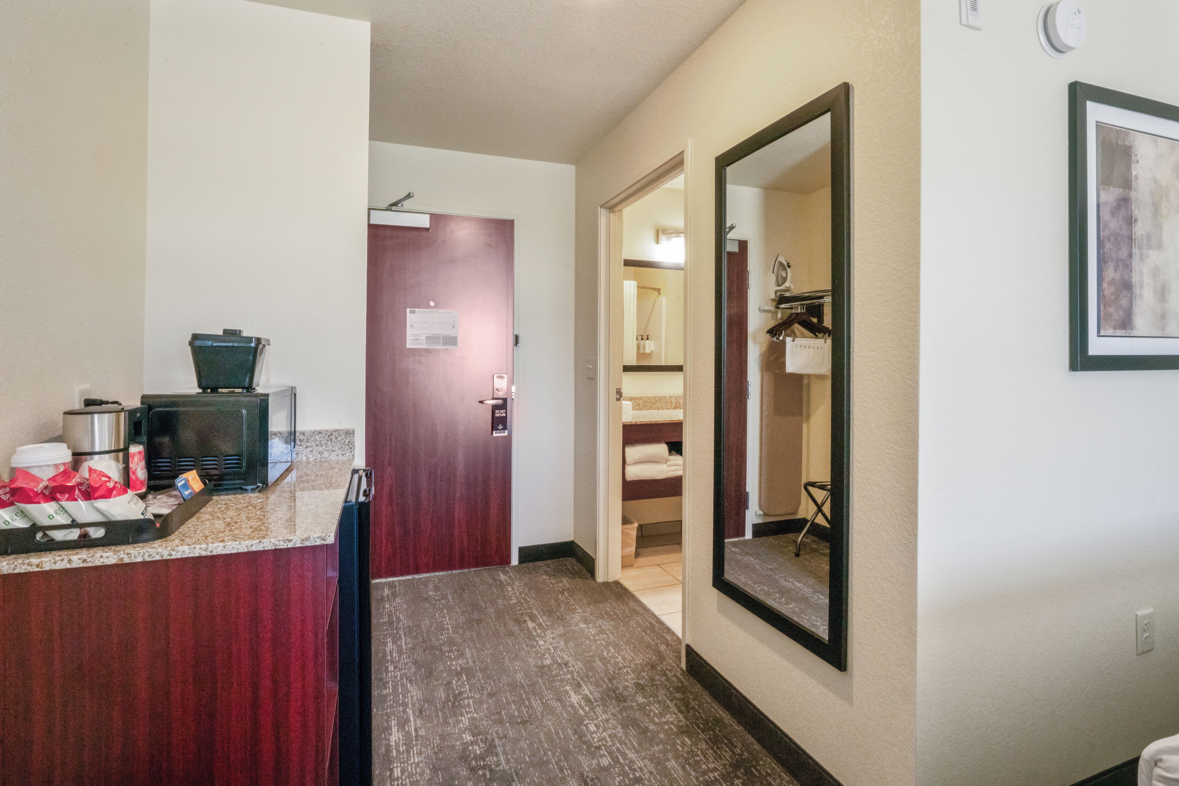 A hotel hallway with a reception area, a mirror, and a door leading to a bathroom.