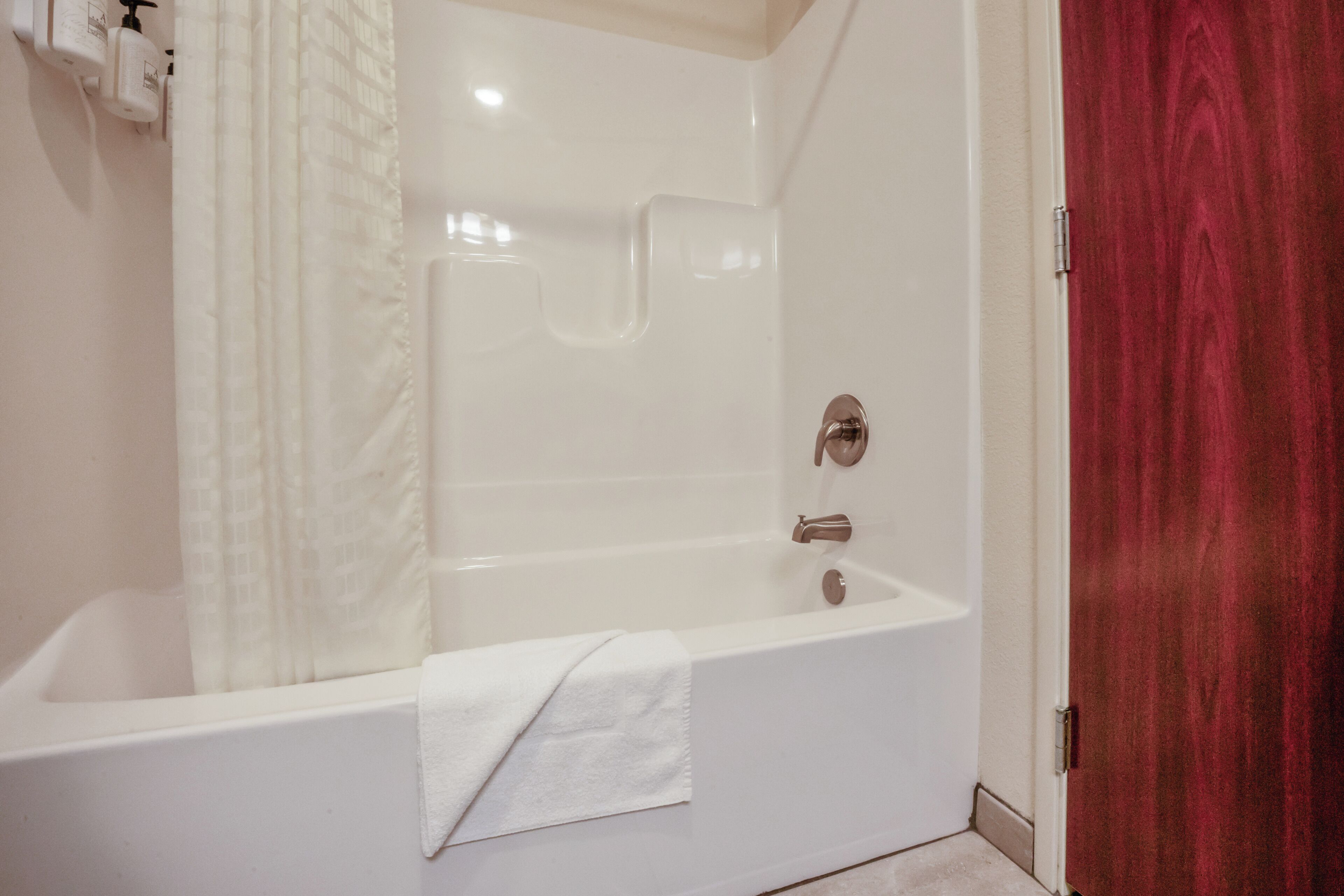 A white bathtub with a shower curtain, a towel, and a red door.