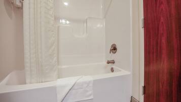 A white bathtub with a shower curtain, a towel, and a red door.