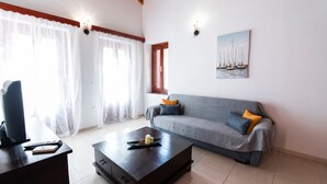 A living room with a sofa, a coffee table, a desk with a computer, and a painting on the wall. - YIAYIA's Central Apartment (Simi Dodecanese)