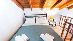 A bedroom with a bed, pillows, a nightstand with a lamp, and a wooden ceiling. - YIAYIA's Central Apartment (Simi Dodecanese)